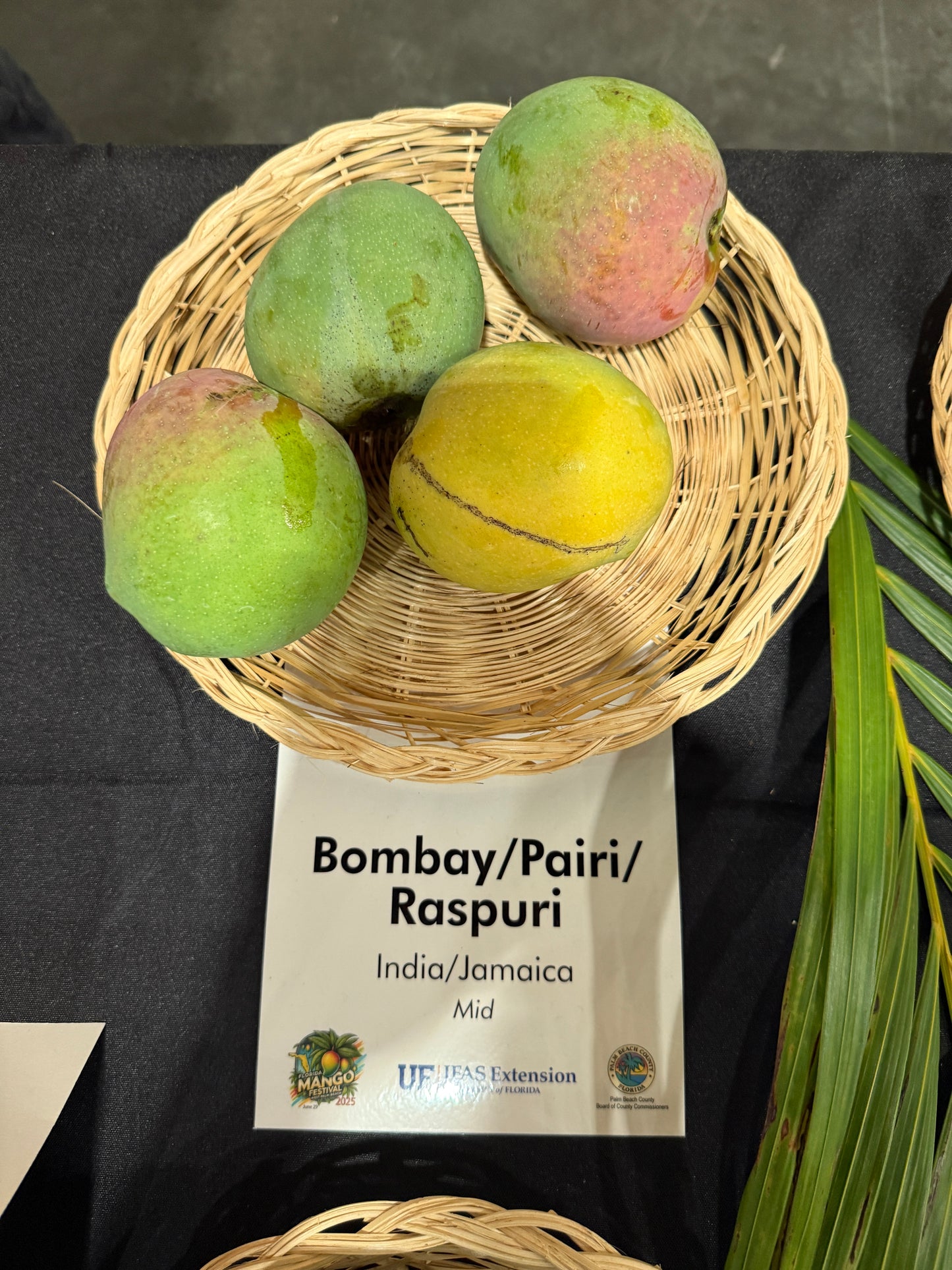 Mangoes in a woven basket with a label on a dark surface